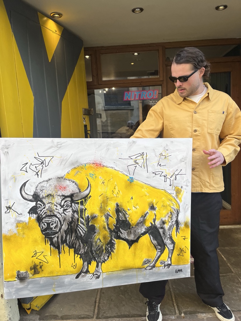 Ben holding his yellow bison painting, black and white line work over a bold yellow ground
