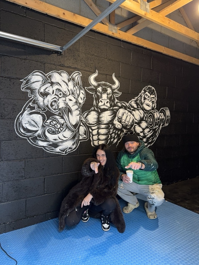 Ben and Niamh crouched in front of their elephant, bull and gorilla gym mural