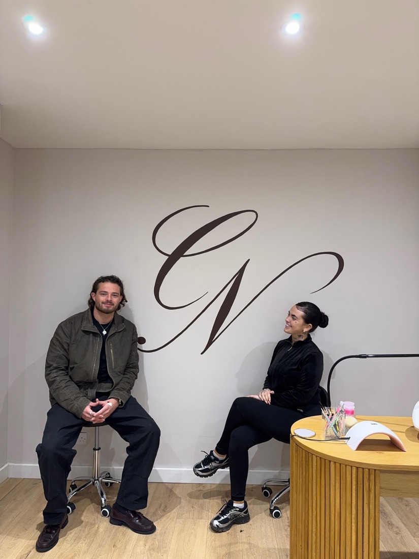 Ben and Niamh seated either side of a hand-painted salon logo
