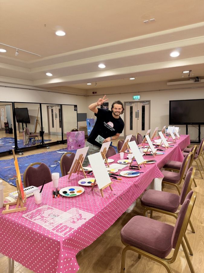 Ben setting up a party art session, easels, canvases and pink tables ready to go