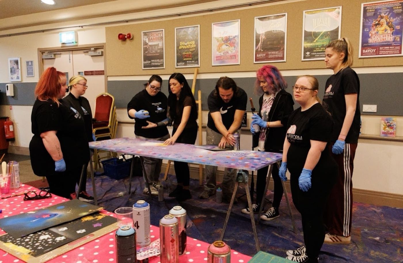 A Patricia Studios inclusive workshop in full flow, a group spray-painting a canvas together with Ben and Niamh